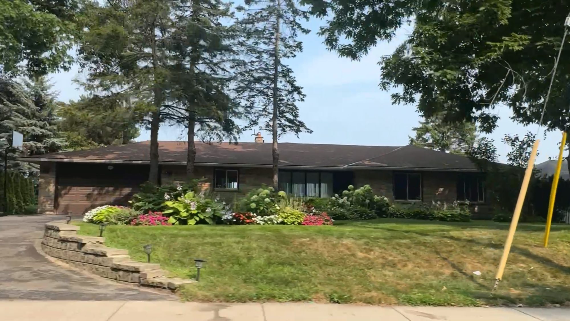 A long bungalow behind a flower border and tall mature trees
