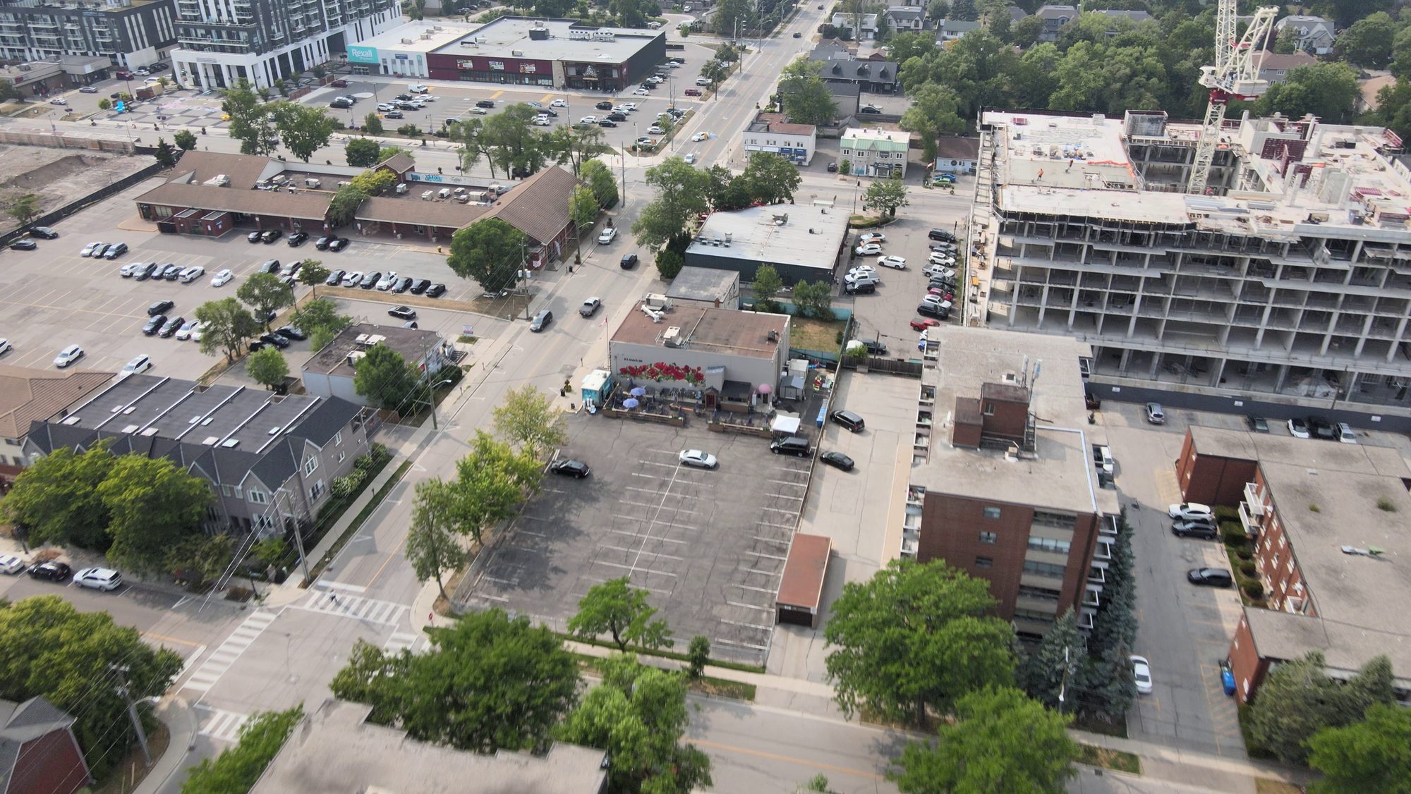 A main road of low commercial blocks with towers rising behind, from the air