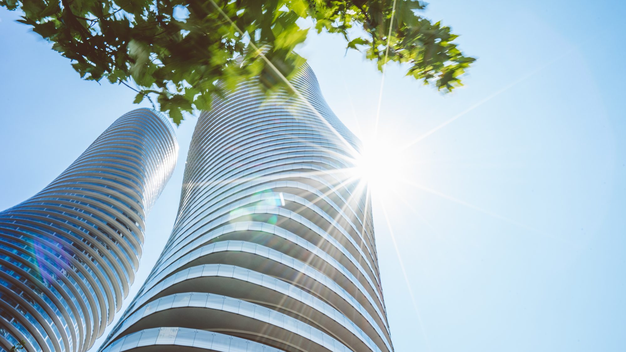 The curved Absolute World towers in Mississauga City Centre seen from below, sun flaring between them